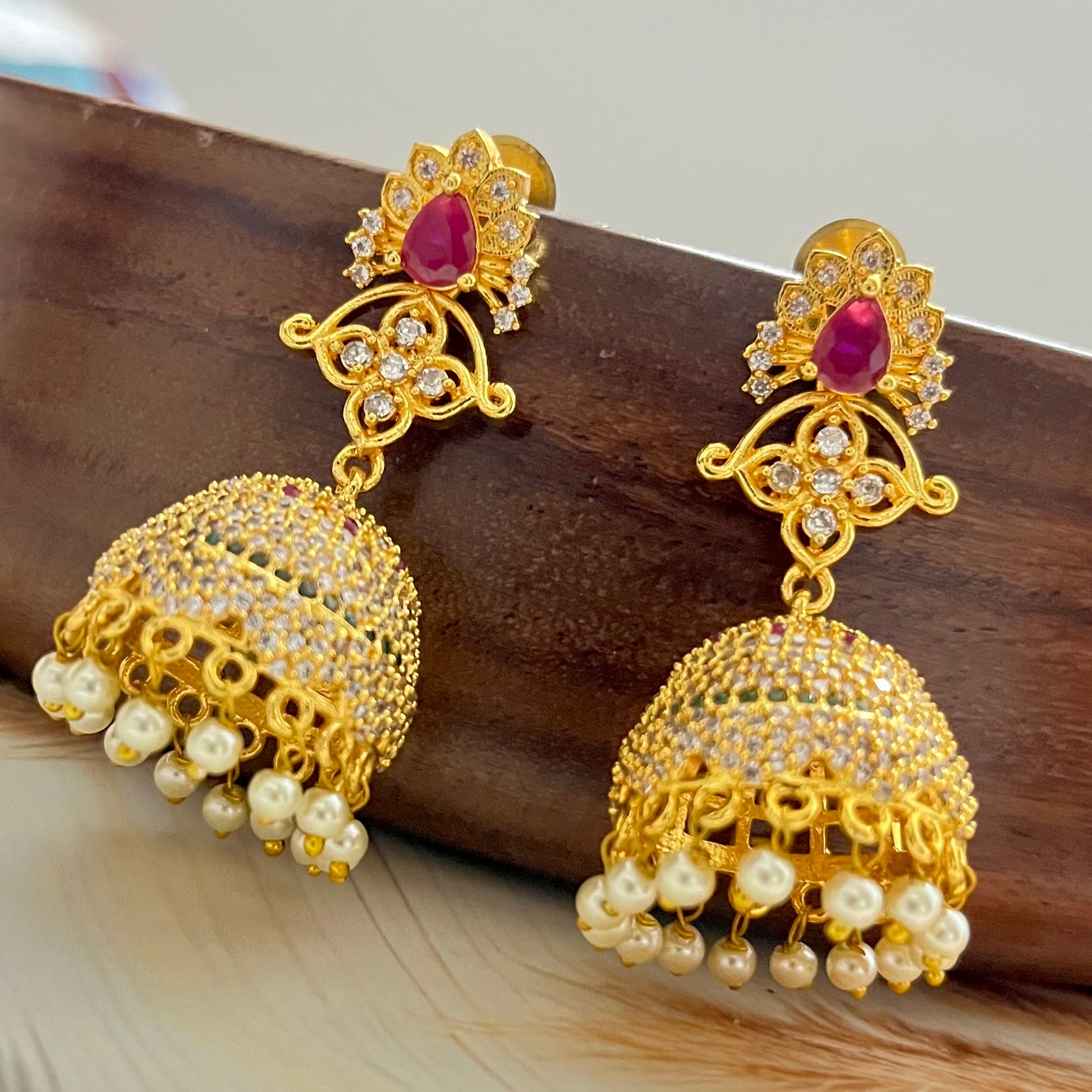 ruby stone jhumka earrings, gold jhumka earrings, traditional jhumka earrings, bridal jhumka earrings, ethnic gold earrings, Indian jhumka earrings, gold plated jhumkas, wedding jewelry for women, temple jewelry earrings, red stone jhumka, pearl drop jhumka, antique gold earrings, festive wear earrings, South Indian jhumka, handcrafted jhumka earrings, CZ stone jhumka, ruby earrings for lehenga, gold earrings for saree, designer jhumka earrings, statement traditional earrings