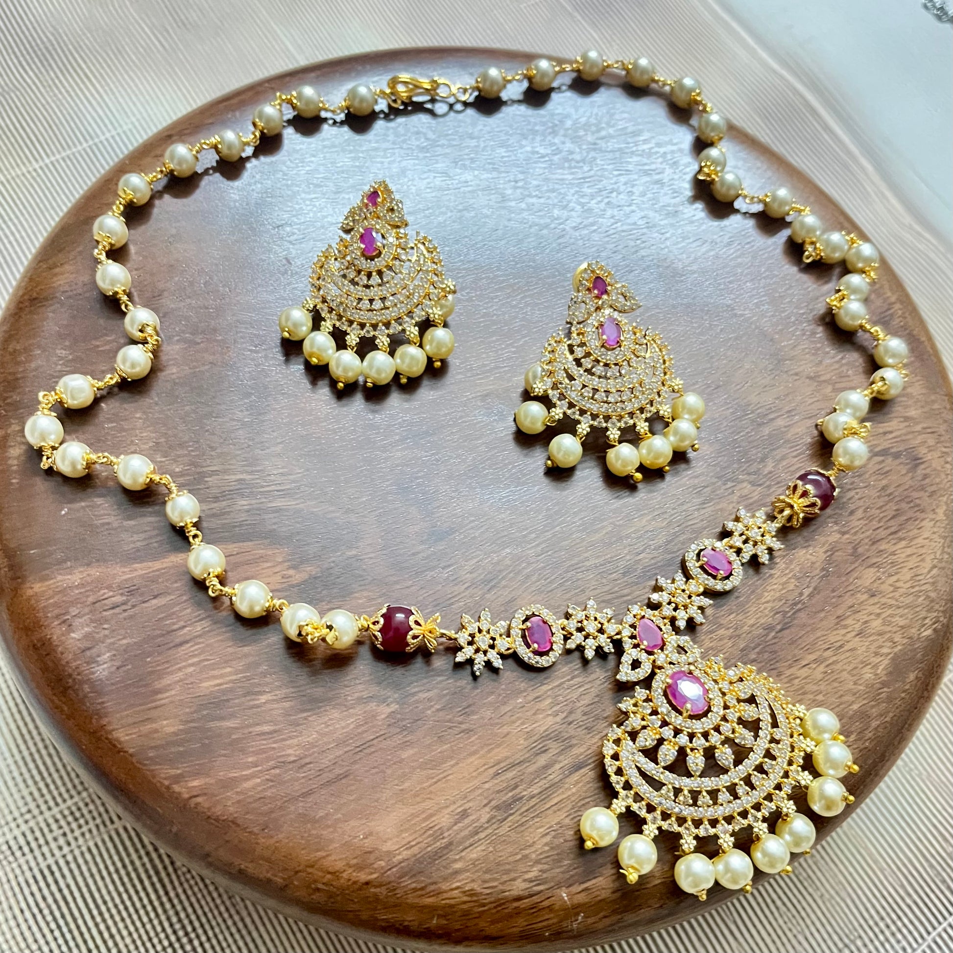 Traditional gold-tone necklace and earrings set with pearls, ruby red stones, and intricate detailing – perfect for festive and bridal wear