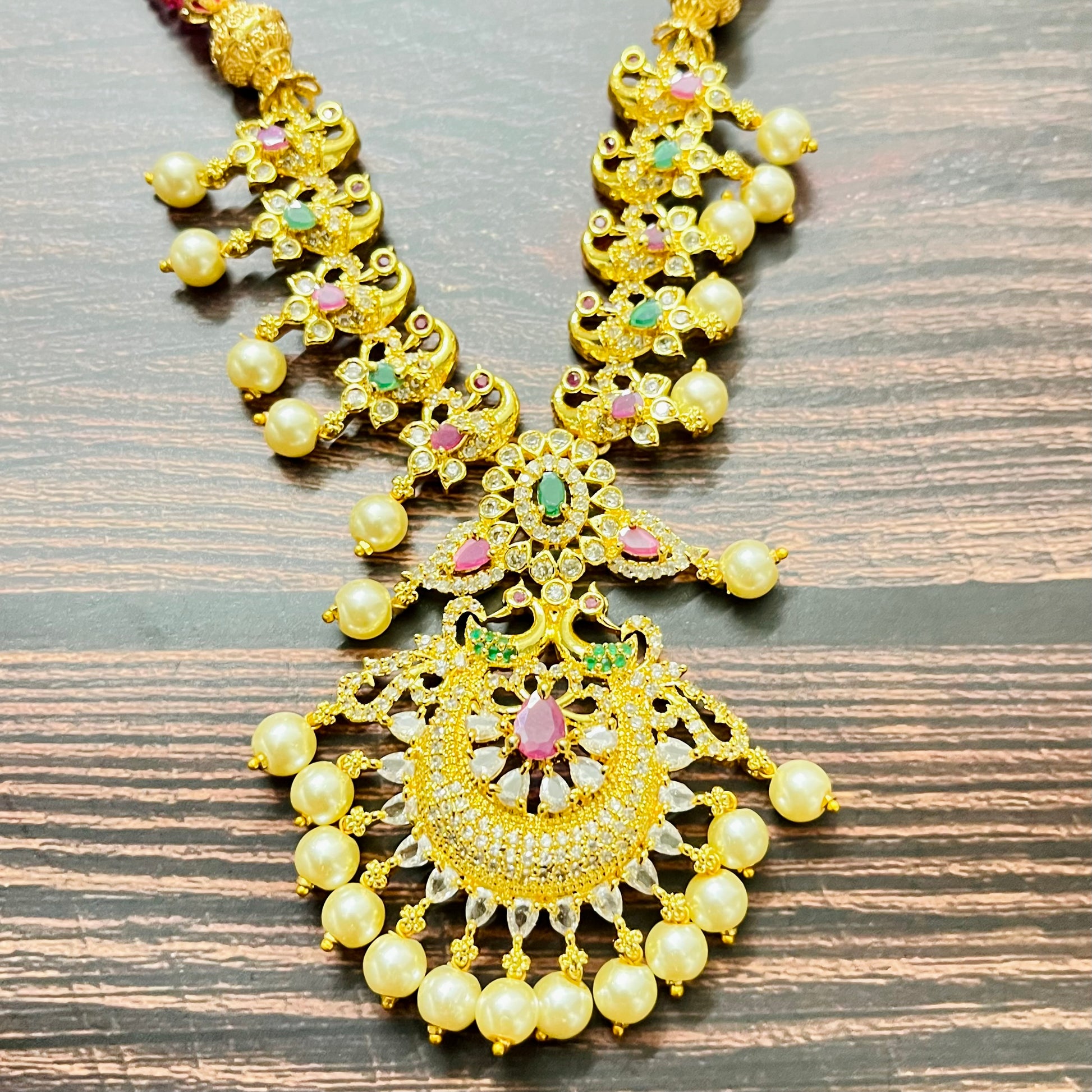 traditional jewelry, temple jewelry, bridal necklace, pearl necklace, ethnic wear, gold plated jewelry, South Indian jewelry, handcrafted jewelry, festive wear, statement necklace, antique finish, Indian bride, designer jewelry, heavy necklace set, wedding collection, navratna stones, ruby emerald combo, temple earrings, kundan work, goddess jewelry, mangalsutra look, cultural heritage, pink thread necklace, handmade jewelry, fashion accessories