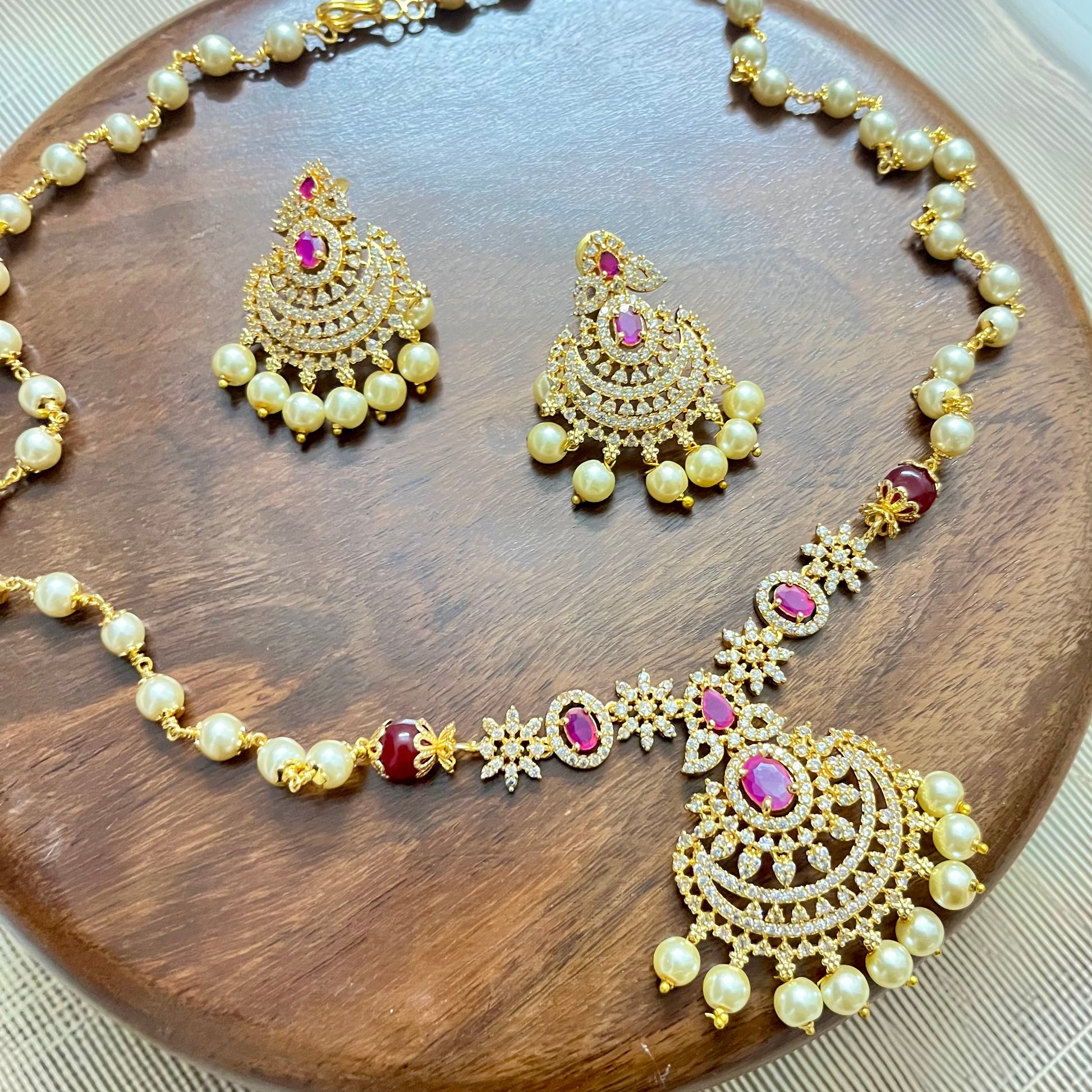 Traditional gold-tone necklace and earrings set with pearls, ruby red stones, and intricate detailing – perfect for festive and bridal wear