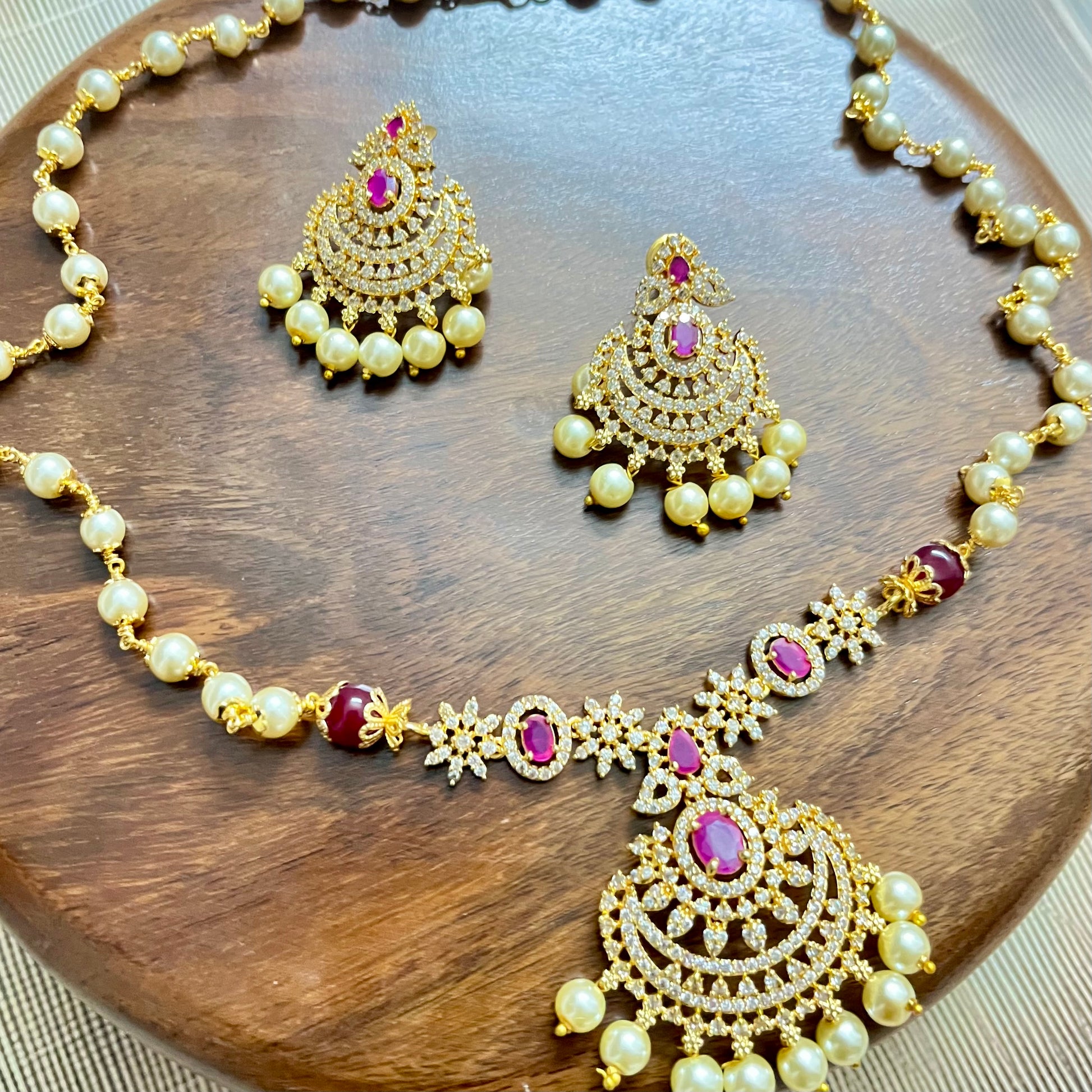 Traditional gold-tone necklace and earrings set with pearls, ruby red stones, and intricate detailing – perfect for festive and bridal wear