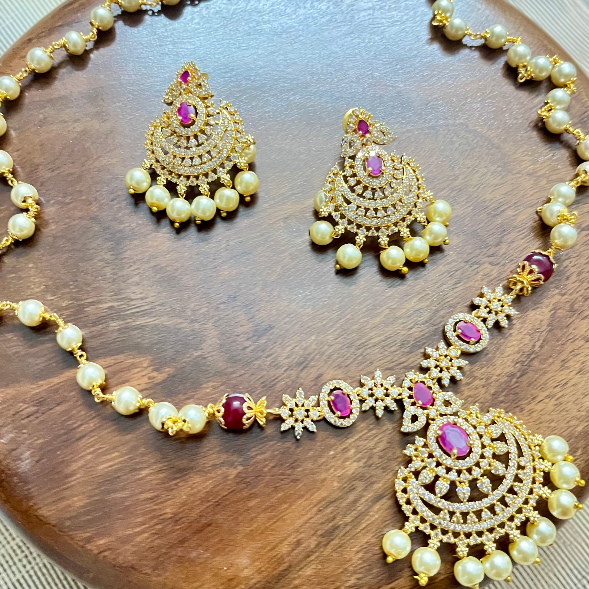 Traditional gold-tone necklace and earrings set with pearls, ruby red stones, and intricate detailing – perfect for festive and bridal wear