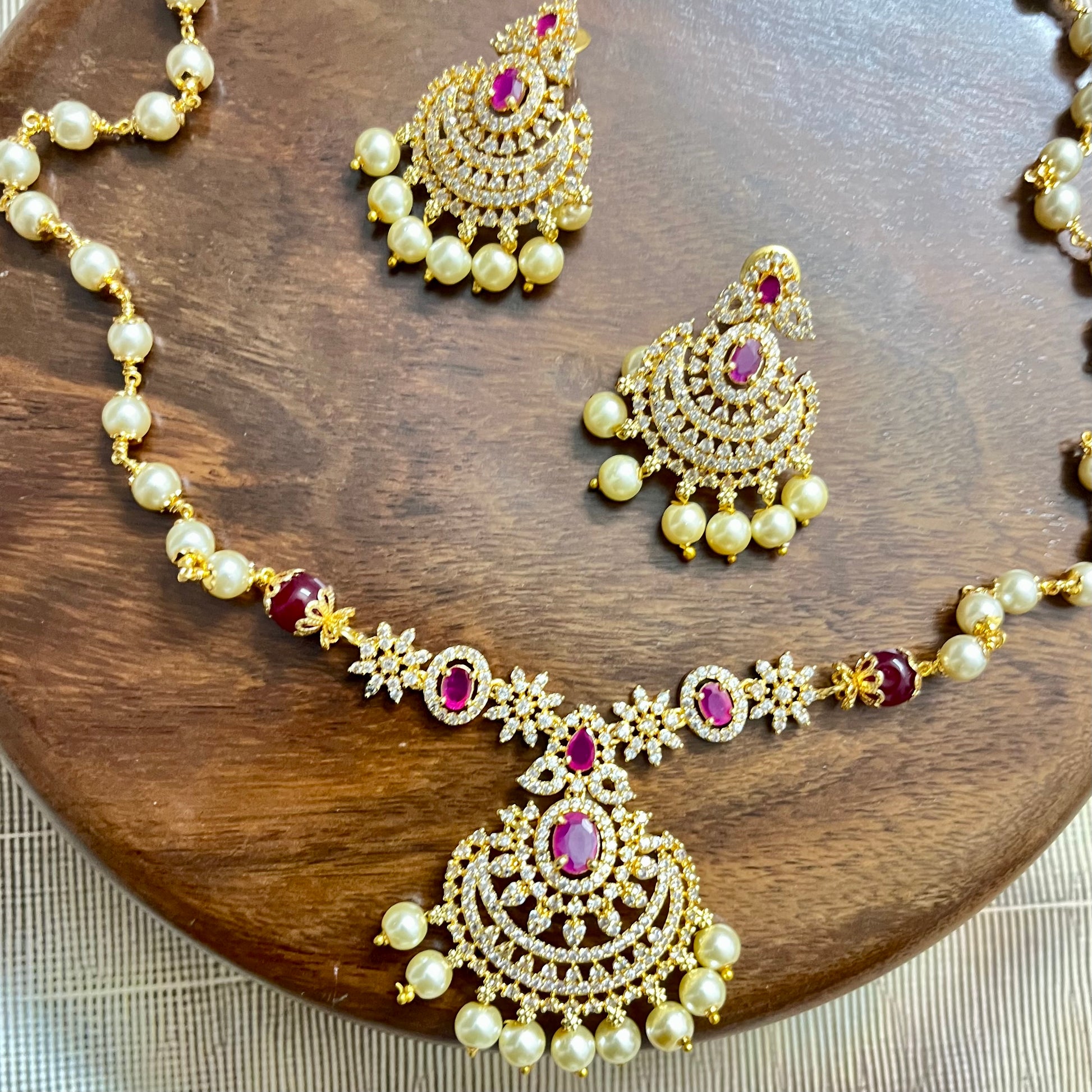Traditional gold-tone necklace and earrings set with pearls, ruby red stones, and intricate detailing – perfect for festive and bridal wear