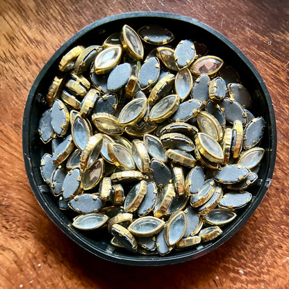 Raw materials for Kundan jewelry making, including uncut stones, gold foil, glass pieces, and other components used in traditional Indian craftsmanship