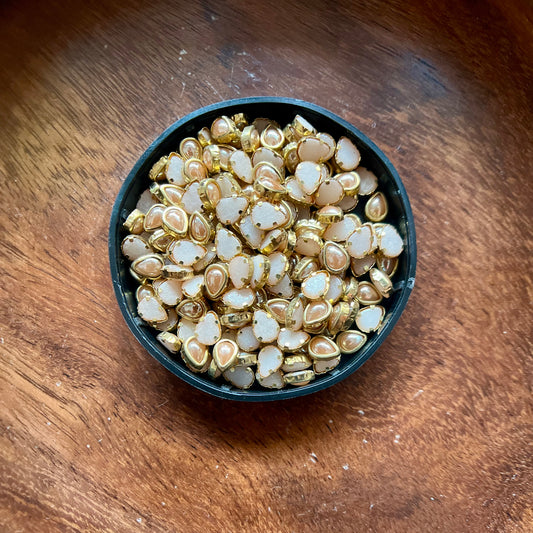 Raw materials for Kundan jewelry making, including uncut stones, gold foil, glass pieces, and other components used in traditional Indian craftsmanship